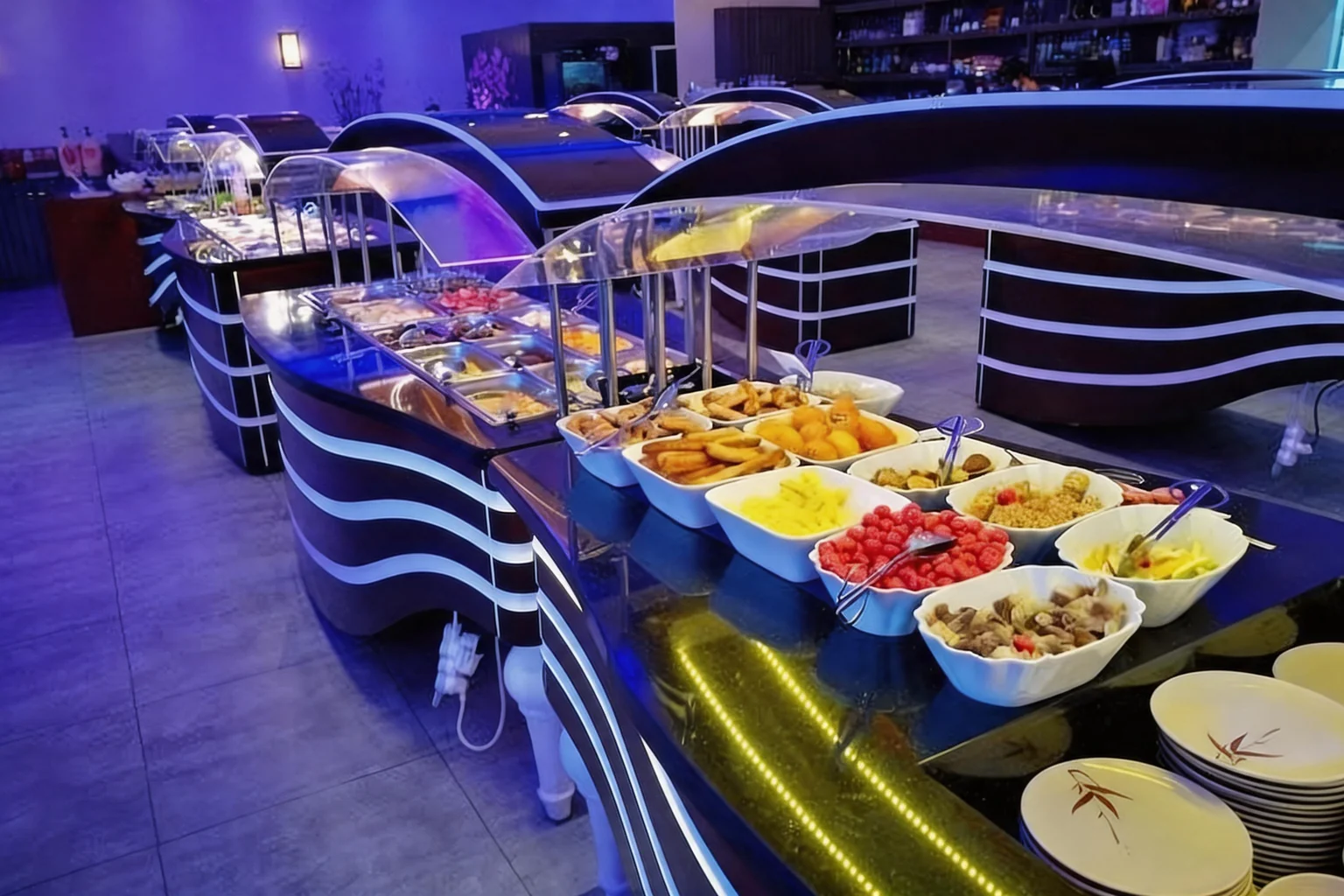 Comptoirs du buffet éclairés en bleu, bols blancs garnis et piles d'assiettes.